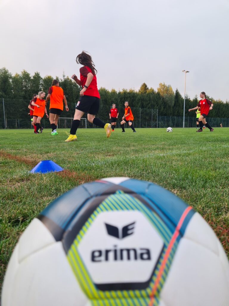 Ein Fußball im Vordergrund und im Hintergrund die FC Perg Ladies beim Training